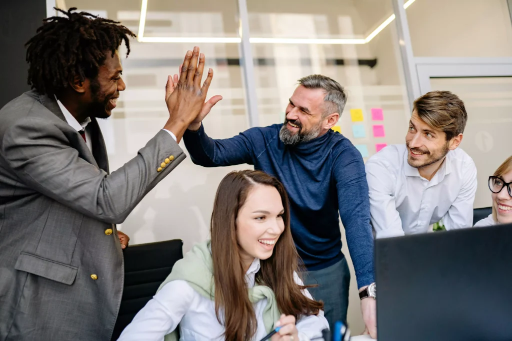 folgas no trabalho: direitos, tipos e boas práticas Equipe diversa celebra com high-five em escritório moderno — cultura organizacional colaborativa
