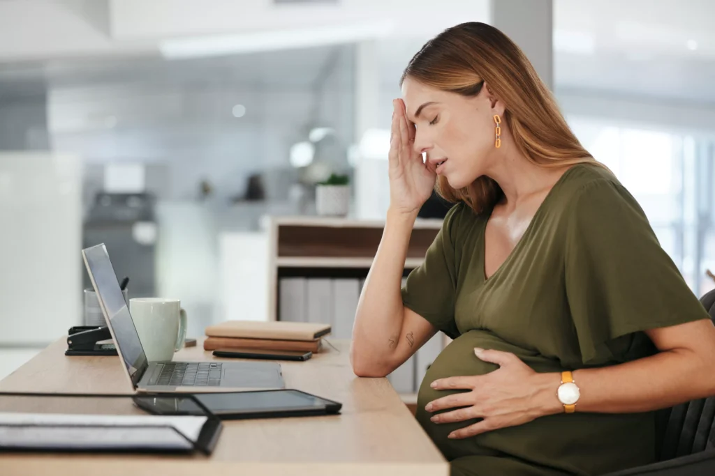 Mulher grávida cansada no trabalho segurando a barriga e a cabeça