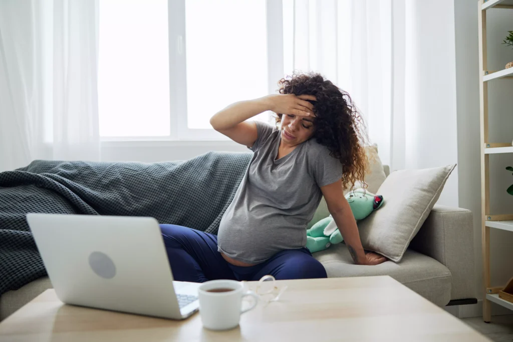 Mulher grávida sentada no sofá com expressão de exaustão