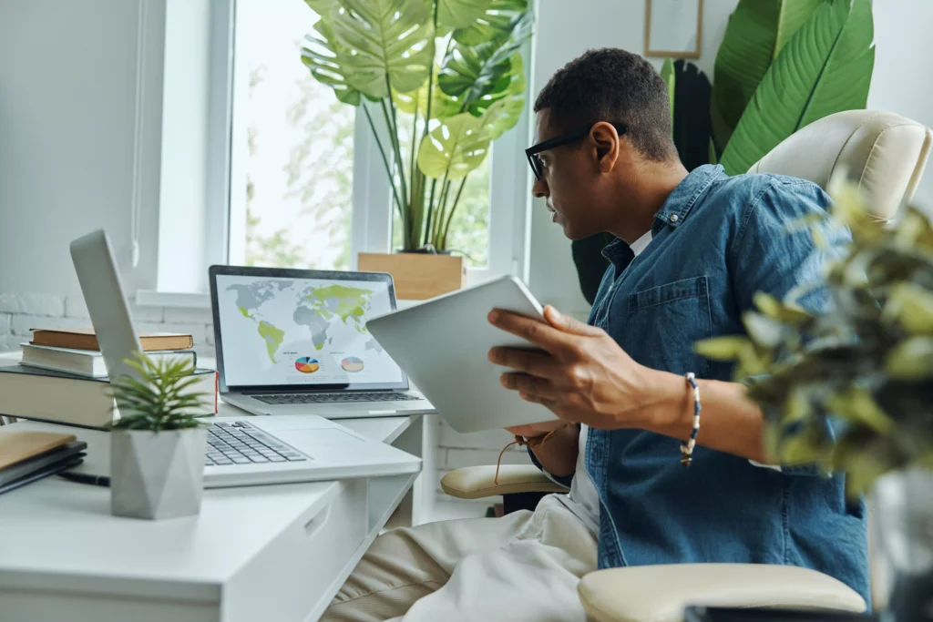 homem trabalhando com tablet e laptop em um ambiente de escritório iluminado, representando flexibilidade no trabalho