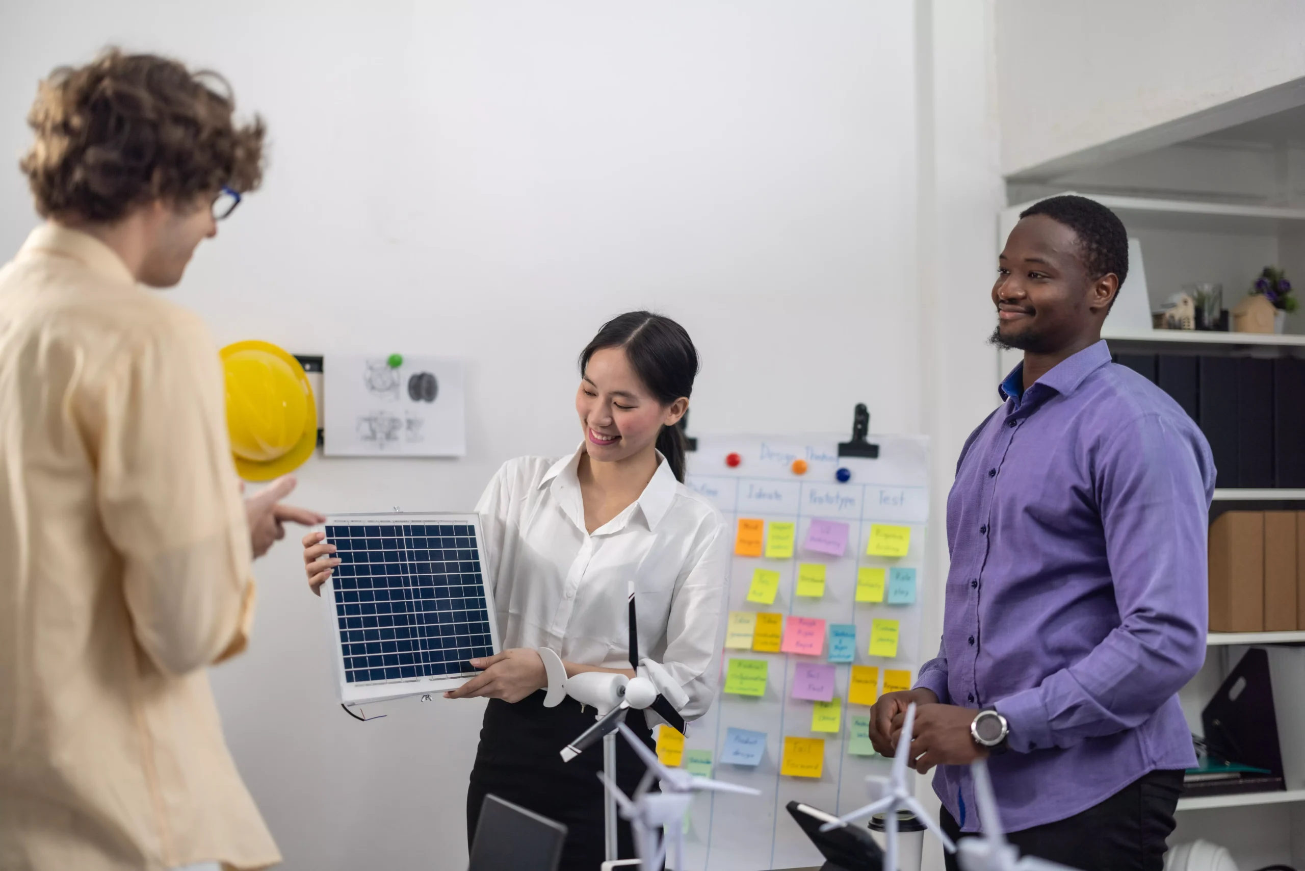 Equipe diversa apresenta painel solar em ambiente de inovação com painéis de ideias e protótipos.
